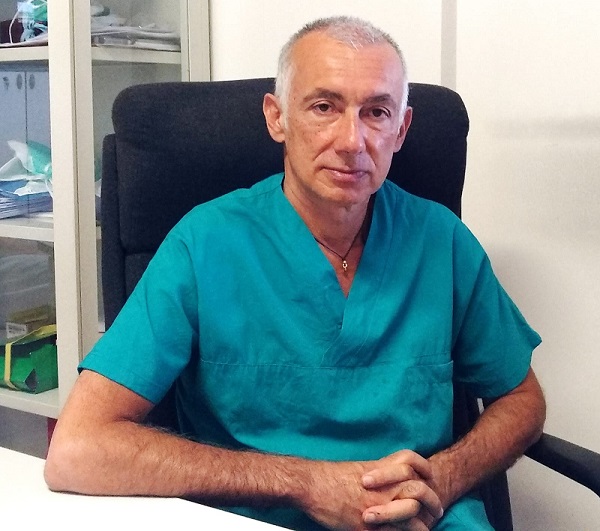 Nella foto il dottor Alessandro Anastasi, seduto su una sedia con il braccio appoggiato alla scrivania. Il medico p vestito di verde. La foto esprime serenità.