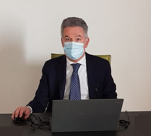 Nella foto il dottor Leonardo Pasquini seduto a una scrivania con un computer portatile davanti. Pasquini ha una mascherina