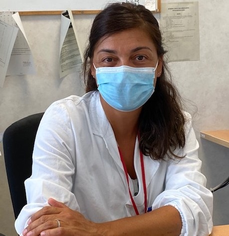 Nella foto la dottoressa Maria Pirrotta, seduta a una scrivania, con mascherina e camice