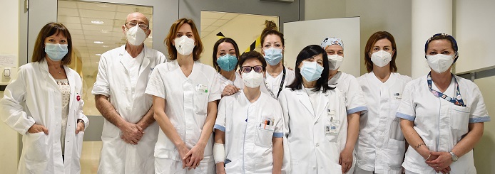 Nella foto medici e infermieri di fronte alla porta del reparto, tutti in divisa e con la mascherina. La foto esprime professionalità